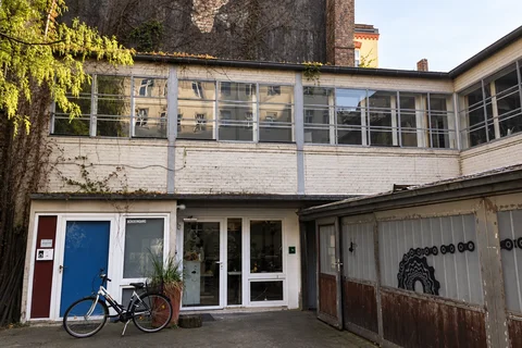 Unser Büro im Innenhof mit großen Fenstern, weißen Backsteinwänden und einem Fahrrad am Eingang.